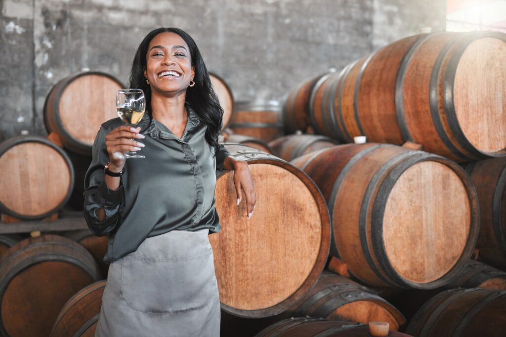 Woman winemaking with a glass with wood barrels of white wine in a winery cellar or di